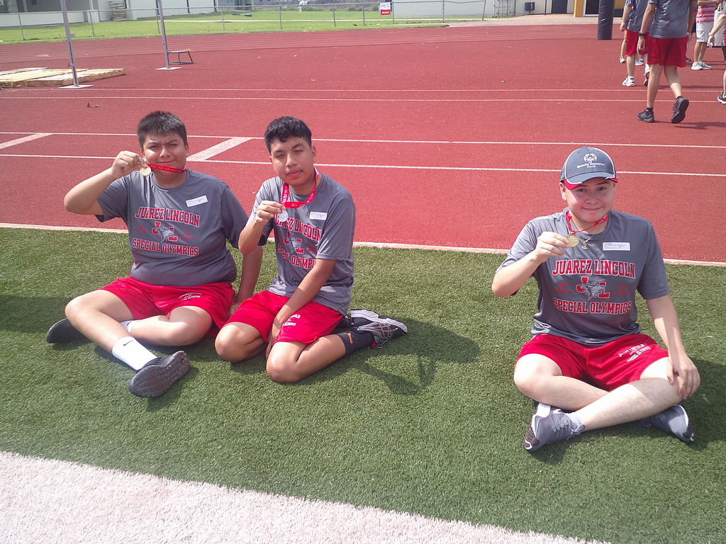 3 students sitting on football field holding up the medals around their necks